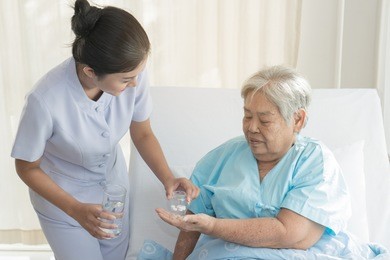 caregiver nurse helping elderly woman taking medicine on the bed and check up after admit inpatient in hospital.