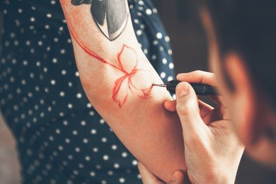 a young guy, a tattoo artist preparing for the session, draws a sketch on the body of the client in a welcoming environment