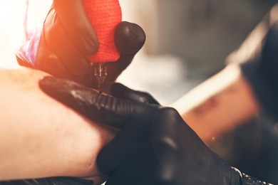 a young guy, beats a tattoo on the hand of the girl in a tattoo parlor, rotary tattoo machine, black ink, lens flare