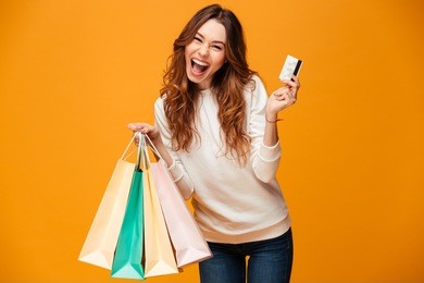 image of excited screaming young woman standing isolated over yellow background looking camera holding shopping bags and credit card.