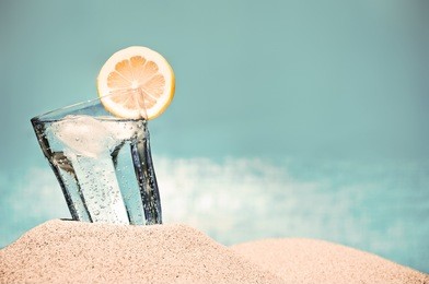 cold drink with ice and a slice of lemon on the beach on a hot summer day