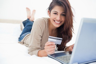 a woman smiling and looking in front of her as she uses her credit card with her laptop.