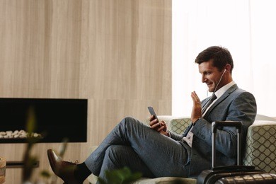businessman sitting at airport lounge making a video call by smartphone. business executive talking and waving during a video call.