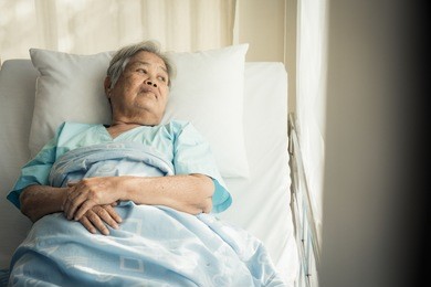 lonely asian elderly female patient lying on the bed in the hospital and looking away outside the window waiting to see her child and her family to visit.