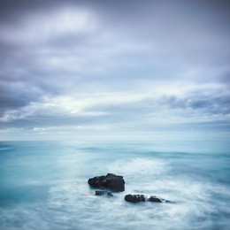 dark rocks in a blue ocean under cloudy sky in a bad weather. long exposure photography