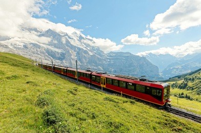 a cog wheel train traveling on famous jungfrau railway from jungfraujoch station ( top of europe ) to kleine scheidegg on a green grassy hillside, in berner oberland ( bernese highlands ), switzerland
