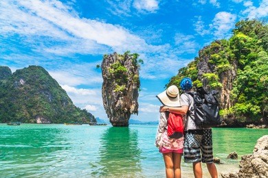 couple travelers with packpack relaxing on sea beach joy view of james bond island, phang nga bay, near phuket, travel in thailand, beautiful destination landscape asia, summer outdoor vacation trip