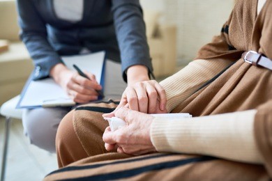 close up of female psychologist holding hand of senior woman during therapy session, copy space