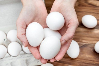 female's hands holding eggs over table with eggs and carton container.