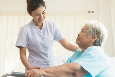cheerful asian nurse visiting elderly patient to check up after surgery in hospital for giving physical therapy and encouragement.
