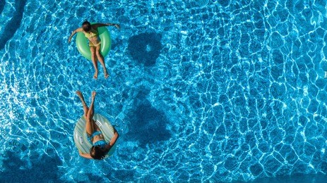 aerial top view of children in swimming pool from above, happy kids swim on inflatable ring donuts and have fun in water on family holiday vacation on resort
