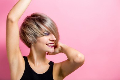 happy cheerful young woman wearing short hair rejoicing looking sideways with joyful and charming smile. beautiful woman in casual outfit over bright pink background dancing