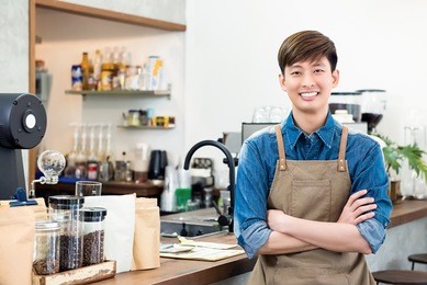 cheerful young asian man entrepreneur standing at counter in his own coffee shop