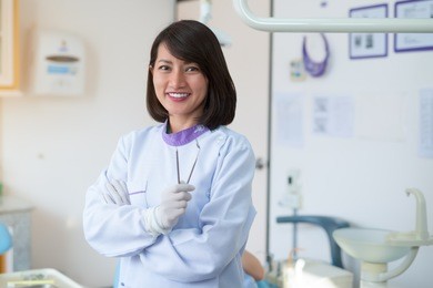 asian woman dentist stood smiling and holding a dental tool in a hospital.