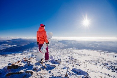 young woman with her back in her hands holds a snowboard, goes to the track for descent from the mountain on fresh snow