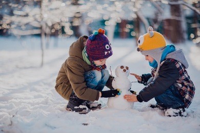 children play outdoors in snow. outdoor fun for family christmas vacation. two little kid boys in colorful clothes playing outdoors. happy siblings having fun with snowman