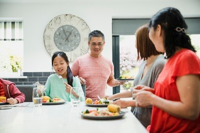 family are sitting down to have their dinner together in the kitchen. they are eating a stir fry.