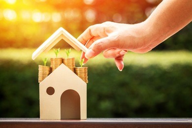 woman hand hold to open a roof and a coin stack substantial savings money inside the house and plant growing on the top in the public park, business investment or loan for real estate concept.