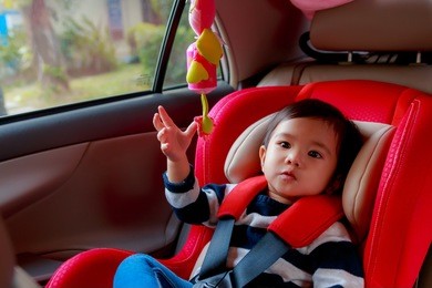 portrait of asian baby girl sit in the red car seat for safety.