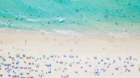 aerial view of sandy beach with tourists swimming in beautiful clear sea water.