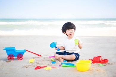 cute little boy playing sand at the beach with sand tools.