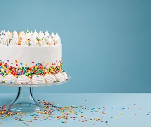 white birthday cake with colorful sprinkles over a blue background.