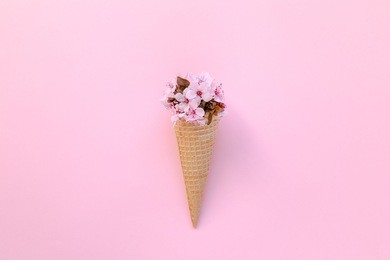 fashion decoration of ice cream cone with pink flowers on top over a pink background, minimalistic design. top view.