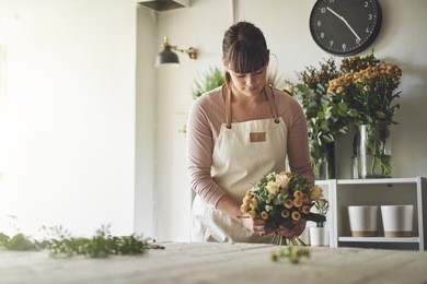 young female florist putting together a bouquet of mixed flowers while working at a table in her flower shop