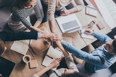 successful team. top view of young business people holding hands together while sitting at the office table together