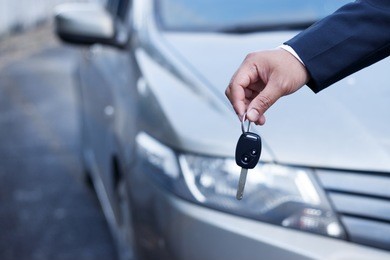business man holding car keys with car on background.