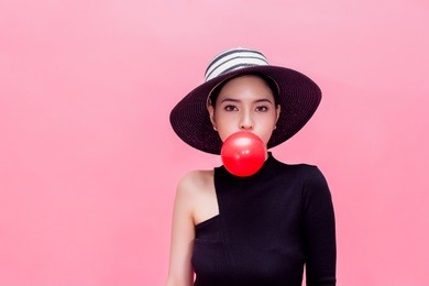 young sweet and attractive woman in luxury fashion lifestyle blowing chewing bubblegum isolated over pink background