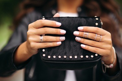 close-up of unrecognizable woman with beautiful trendy manicure wearing wedding set and jewelry holding small black fancy handbag.