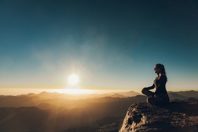 woman sits in a pose of yoga on edge of cliff on mount sinai and meditates against background of beautiful sunrise in egypt.