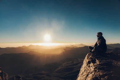 man sits in a pose of yoga on edge of cliff on mount sinai and meditates against background of beautiful sunrise in egypt.