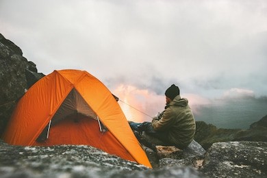 man traveler relaxing in mountains near of tent camping gear outdoor travel adventure lifestyle concept hiking active vacations 