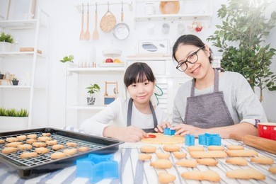 portrait of little asian girl and her mother baking cake and cookies in the kitchen. happy asian family and motherâ??s day concept