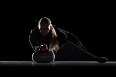 curling player delivering a stone on a curling rink, sliding over the ice, isolated on the black background. curling match curler athlete winter sport. curling match curler athlete winter sports women