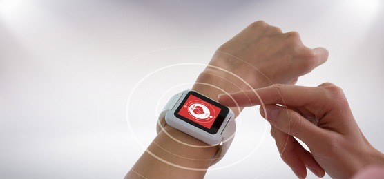 cropped image of hands using smart watch against digital composite of heart icon