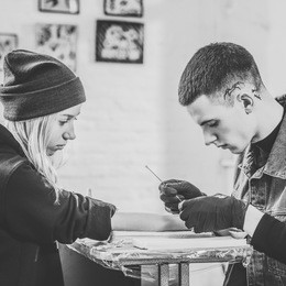 black and white photo of tattoo artist in gloves working on female arm piece in studio
