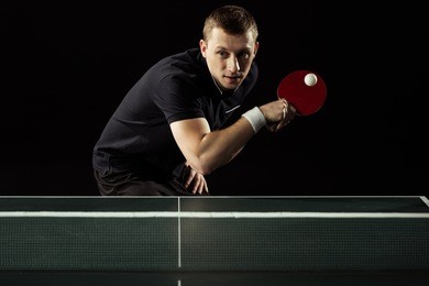 focused tennis player playing table tennis isolated on black
