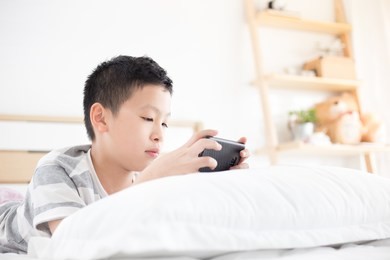 asian boy playing games online  with his smart phone, he feel fun and happy on his bed , games addict problem