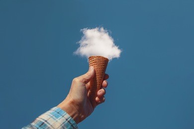 hand holding a sugar cone in front of a fluffy white cloud toned with a retro vintage instagram filter
