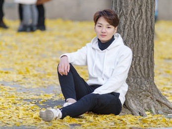 young chinese smiling man portrait sitting in foliage in autumn park. outdoor.