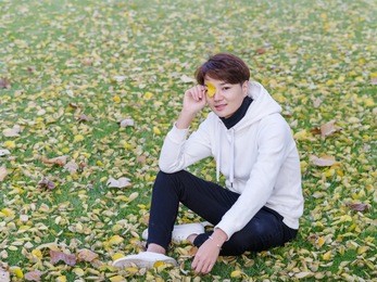 young chinese smiling man portrait sitting in foliage in autumn park. outdoor.