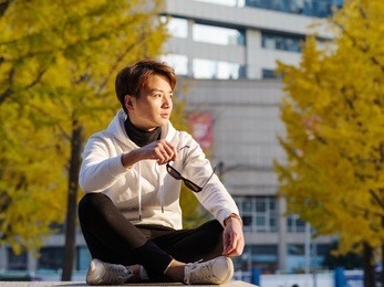 young chinese smiling man portrait sitting with blur yellow trees backgroundin sunset in autumn park. outdoor.