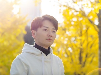 young chinese smiling man portrait stand with blur yellow trees background in sunset in autumn park. outdoor.
