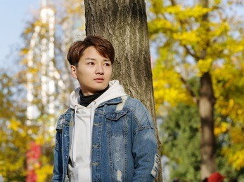 young chinese smiling man portrait stand with blur yellow trees background in sunset in autumn park. outdoor.