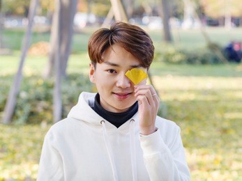 young chinese smiling man portrait stand with blur yellow trees background in sunset in autumn park. outdoor.