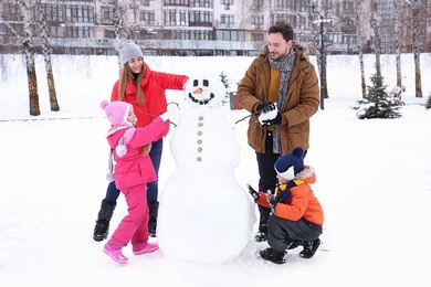 happy family making snowman in park on winter vacation