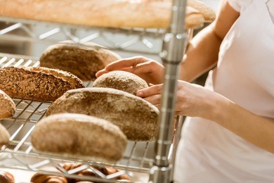 cropped shot of female baker doing examination of freshly baked bread loaves on baking manufacture